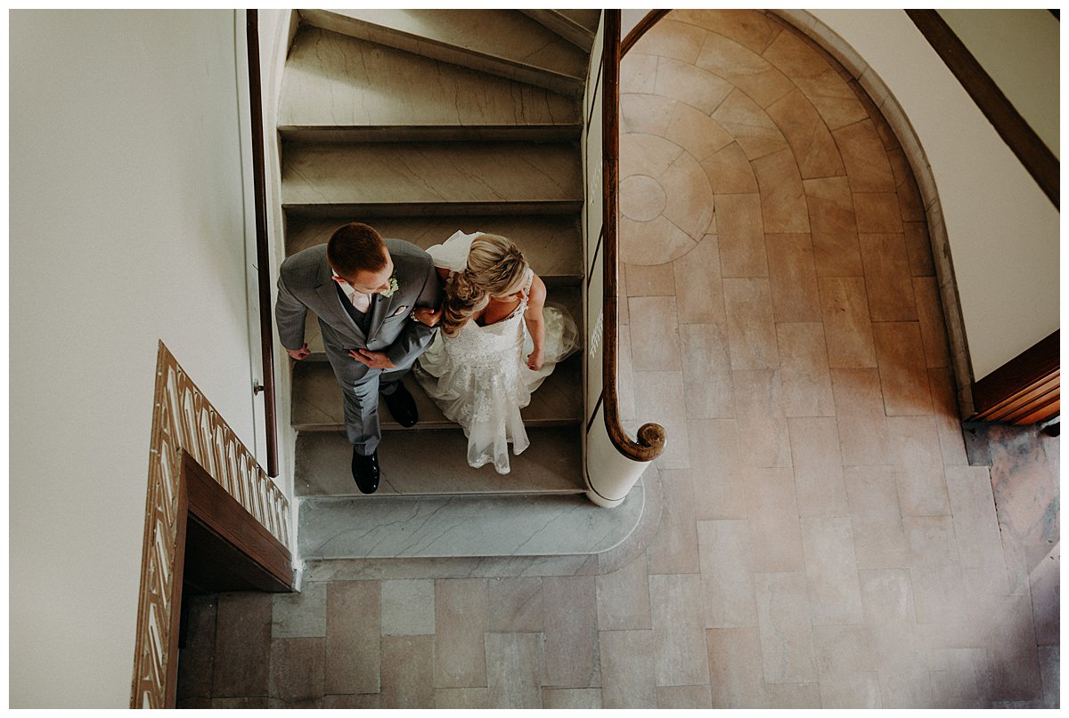 An overhead shot of a bride and groom walking down a set of winding marble stairs who had thier wedding just before the coronavirus pandemic. 