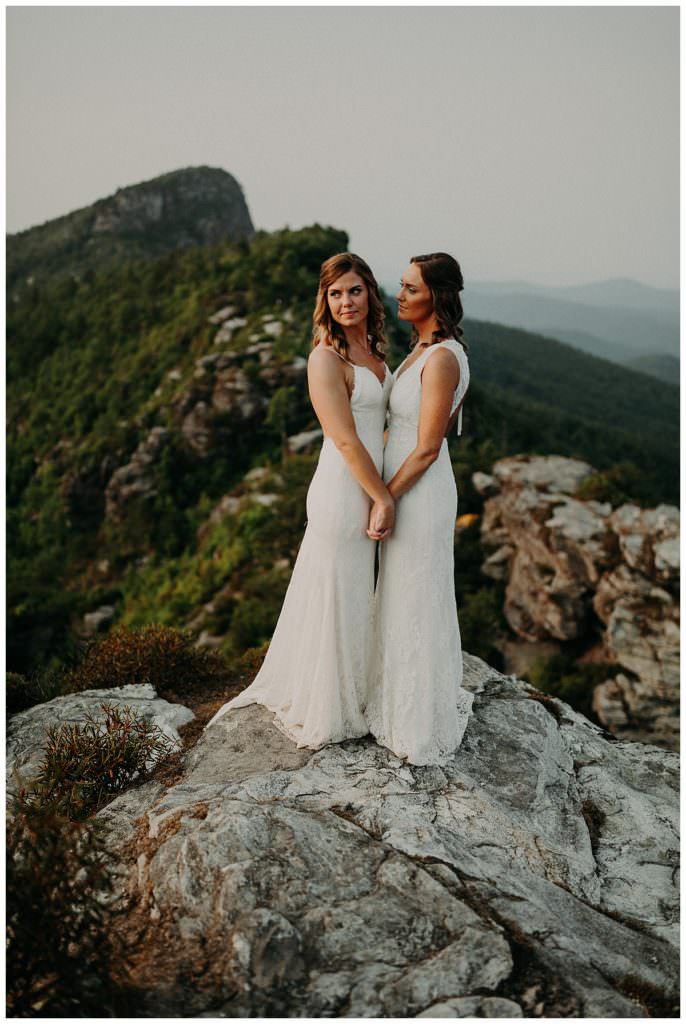 Two brides on an adventure elopement holding hands and looking over a cliff's edge.