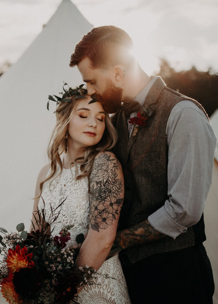 An Asheville elopement photographer captured an incredible backlit image of a tattooed couple eloping at a glamping campground. The image links to the photographer's elopement portfolio.