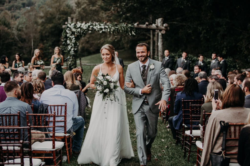 An Asheville wedding photographer captured a beautiful shot of a bride and groom under a flower trellis. The purpose of the image is to share a review of his Asheville wedding photography services.